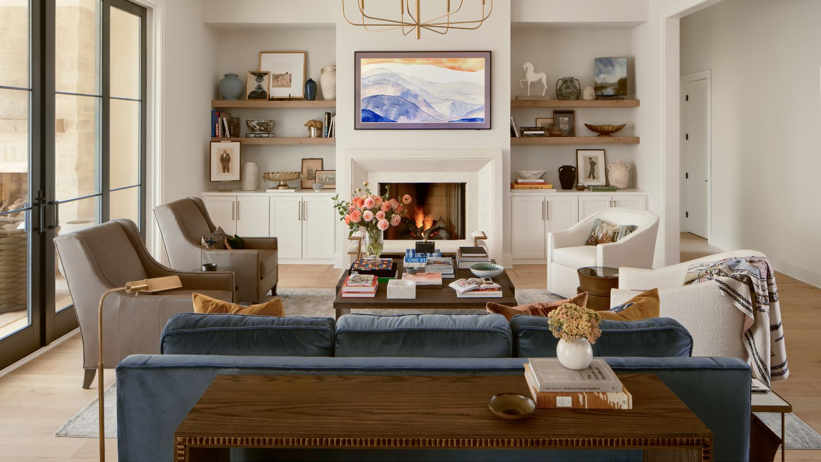 neutral living room with a fireplace, built in cupboard and shelves in the alcoves, a blue velvet couch with two boucle swivel chairs