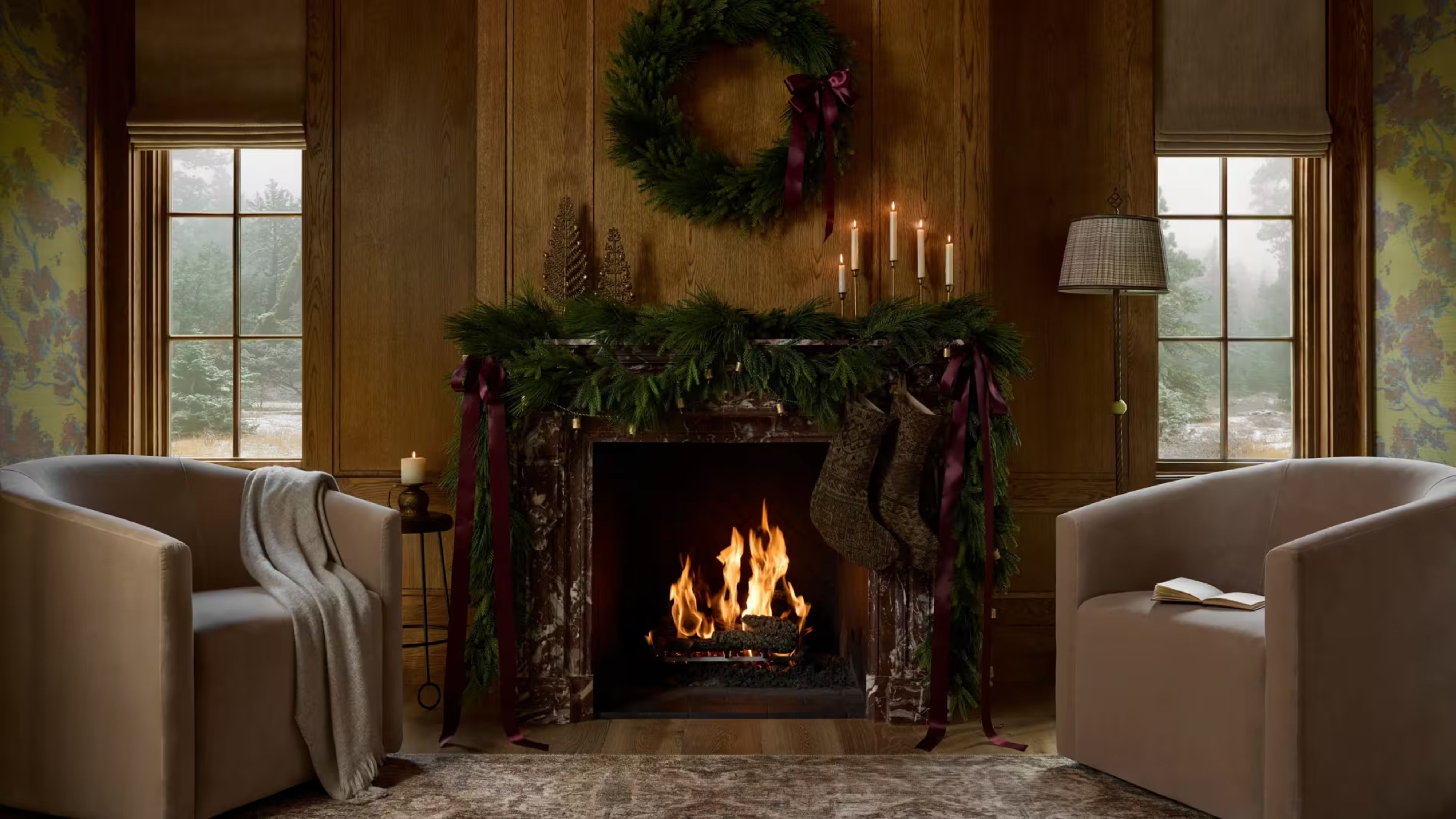 Cozy, festive living room featuring a roaring fire styled with garland and a Christmas wreath overhead. Two sitting chairs flank the wood-paneled scene.