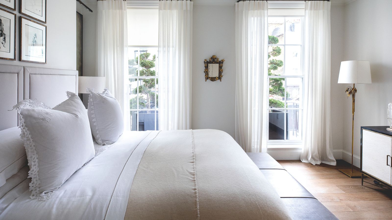 Neutral bedroom with bed in foreground and floor to ceiling windows with sheer drapes