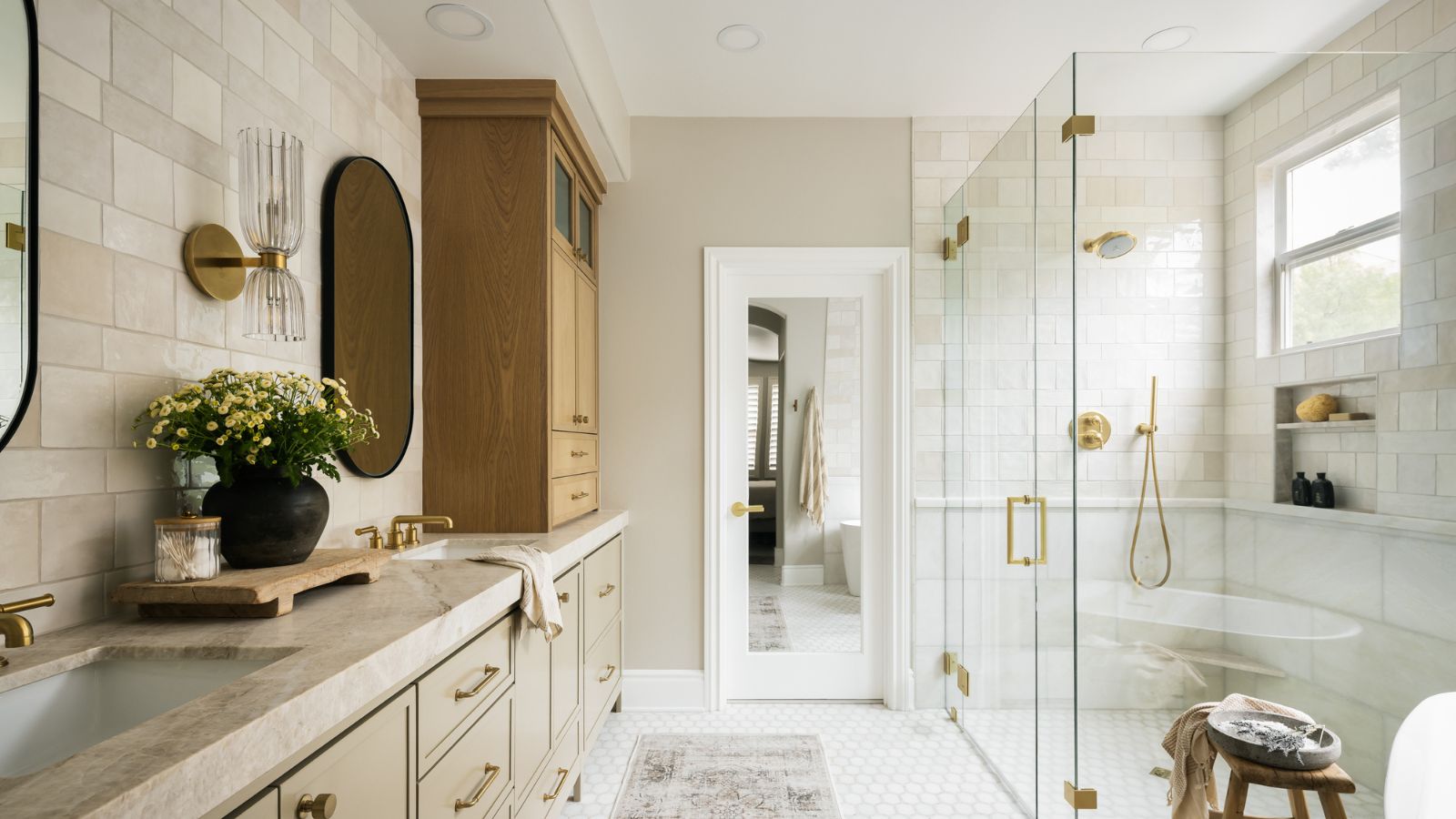 A large neutral bathroom with a taupe vanity, black pill-shaped mirrors, and glass vanity lights