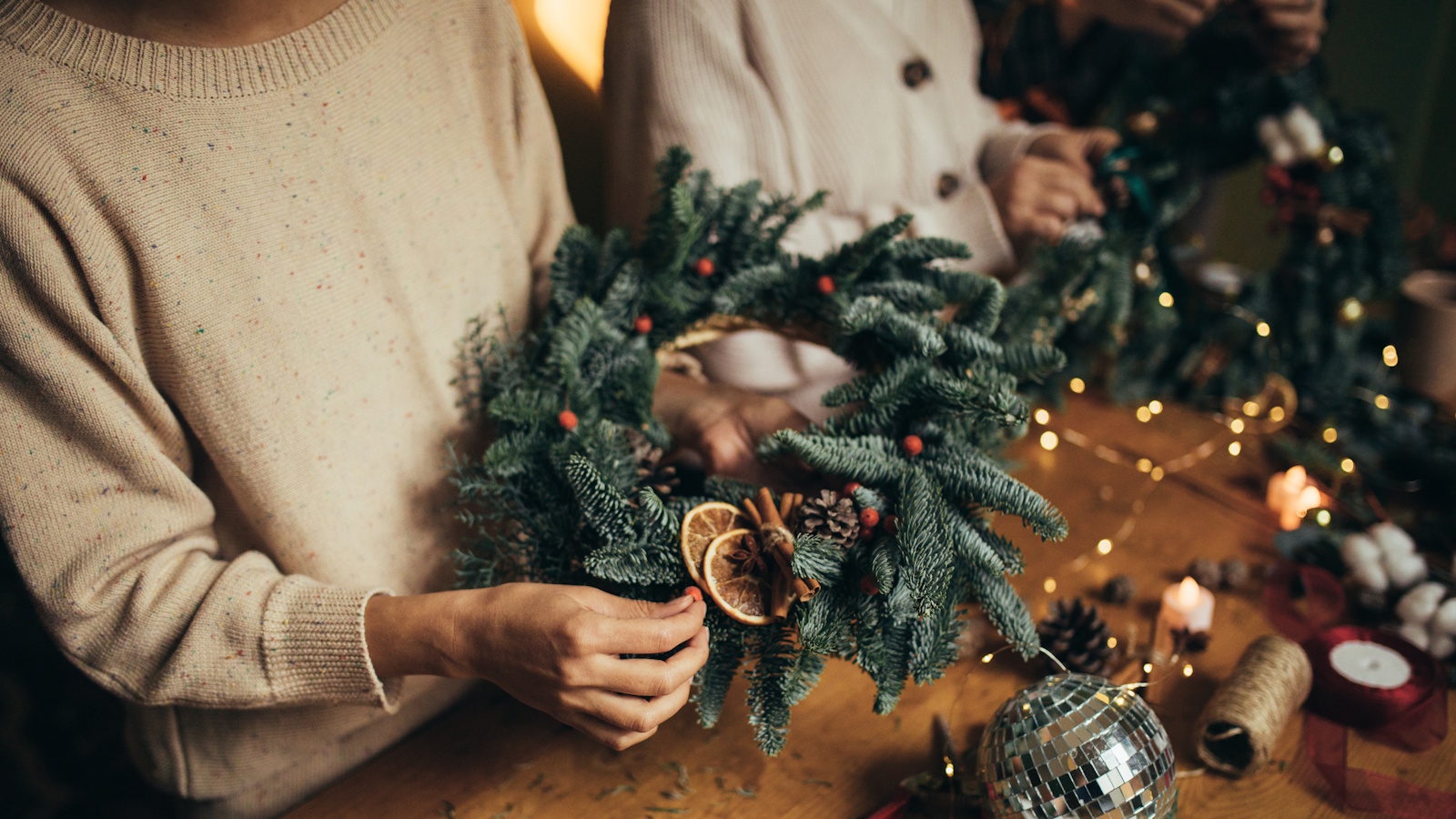 Homemade Christmas wreath being held above wooden crafting table