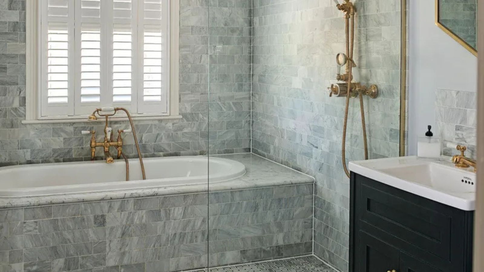 A gray bathroom with a tiled bath and a gold shower faucet