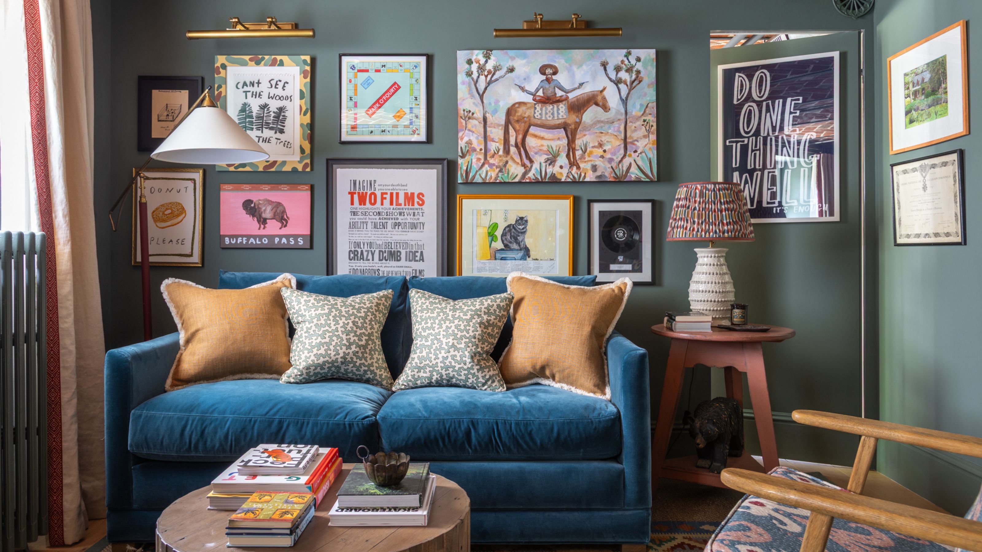 Living room with dark teal walls, blue velvet sofa and a colorful gallery wall
