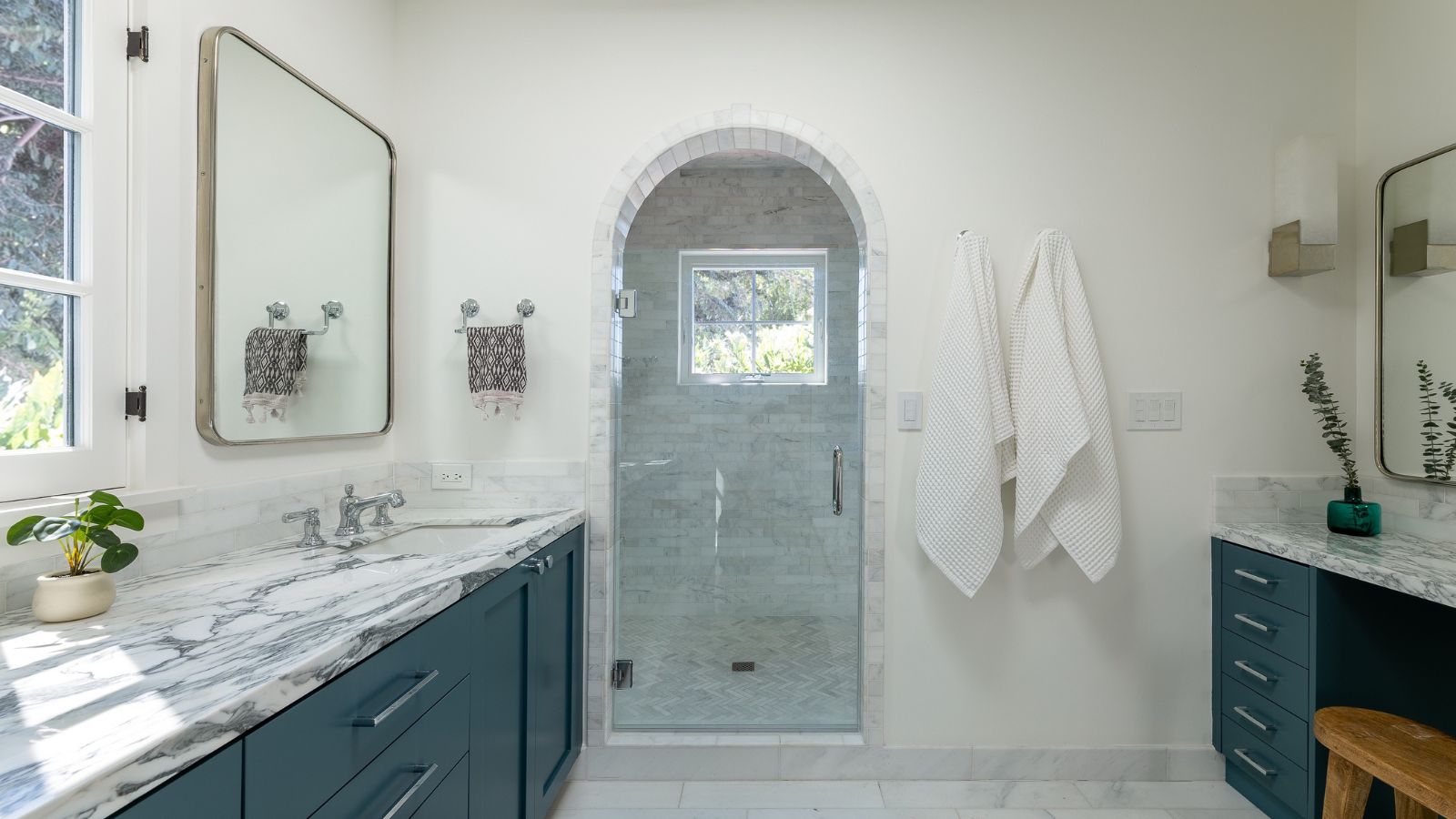 A white bathroom with dark blue vanities and marble countertops
