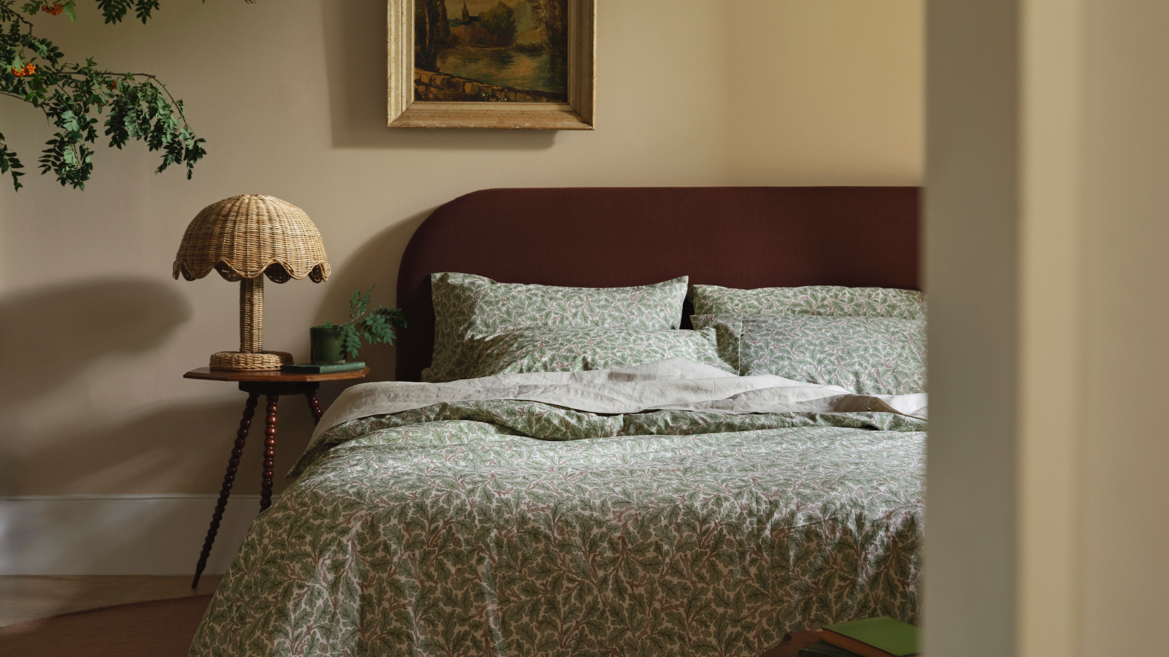 Piglet in Bed x Morris & Co. botanically patterned bedding styled in a neutral bedroom alongside a scalloped rattan table lamp and wall art