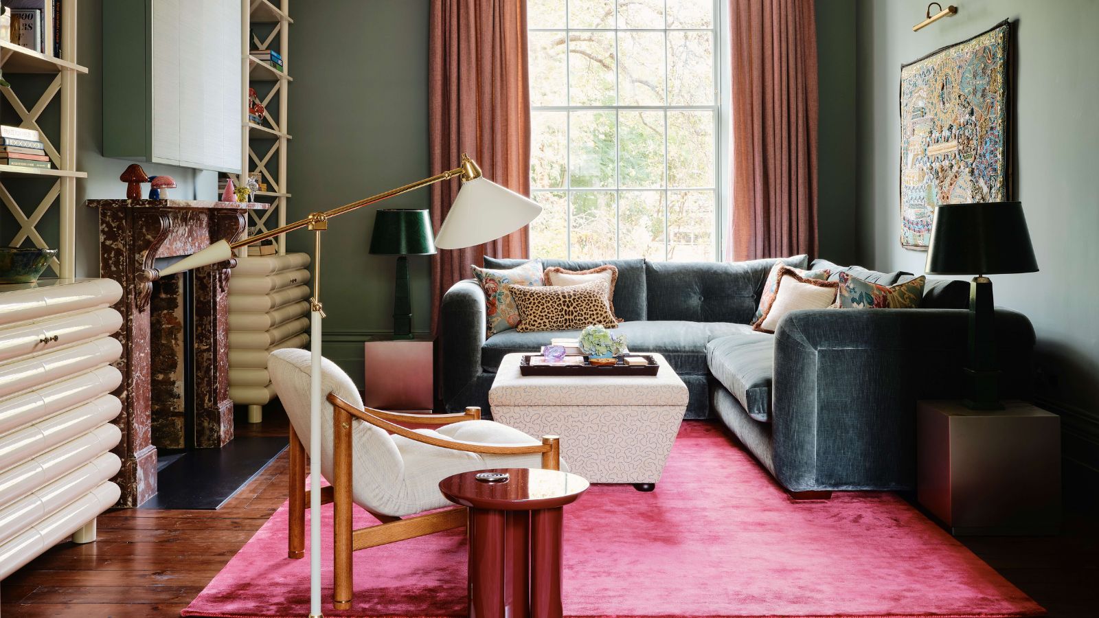 earthy green living room with a large window, vibrant pink deep pile rug with a large green corner couch, small ottoman and a red marble fireplace