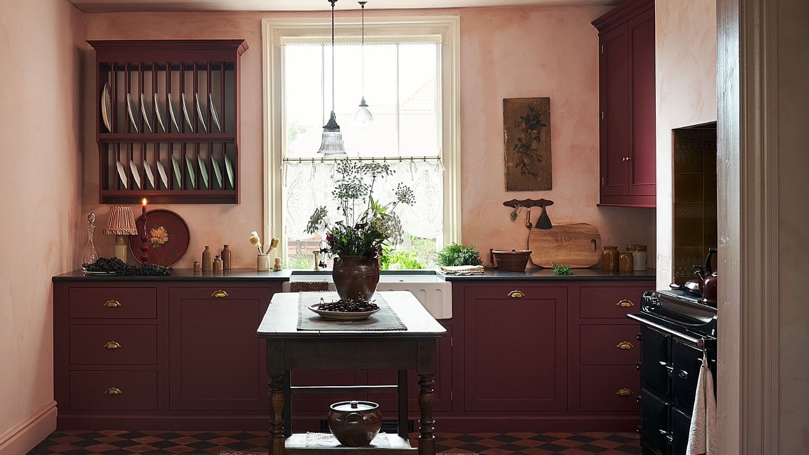 A small kitchen with textured walls, wine red cabinets, and a wooden freestanding island